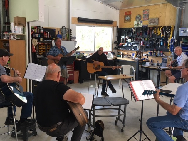 Group of middle-aged men playing guitars in a circle indoors