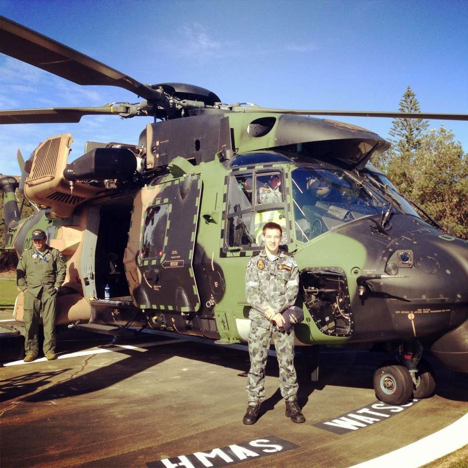 Dean Marchini standing in front of a military helicopter. He is wearing camouflage uniform.