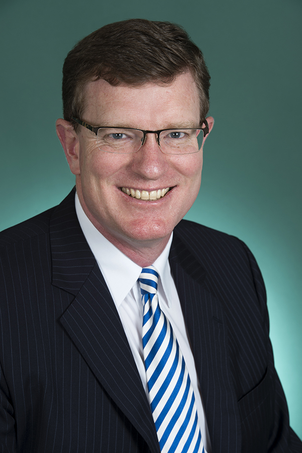 Studio portrait photo of middle aged man smiling and wearing a suit.