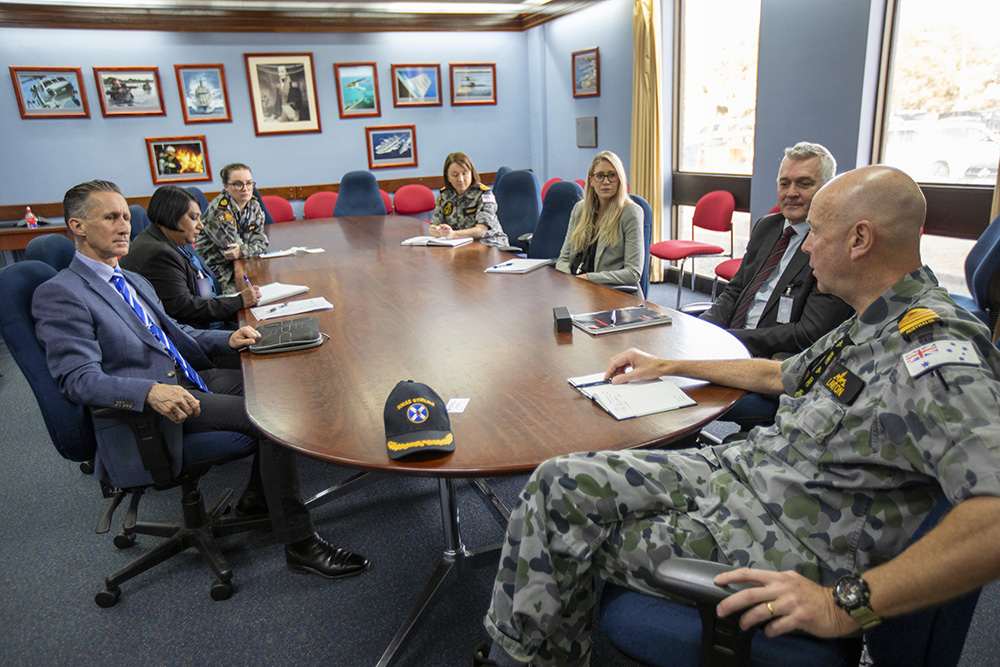 Seven people sitting around conference table, three of them in Navy uniforms.