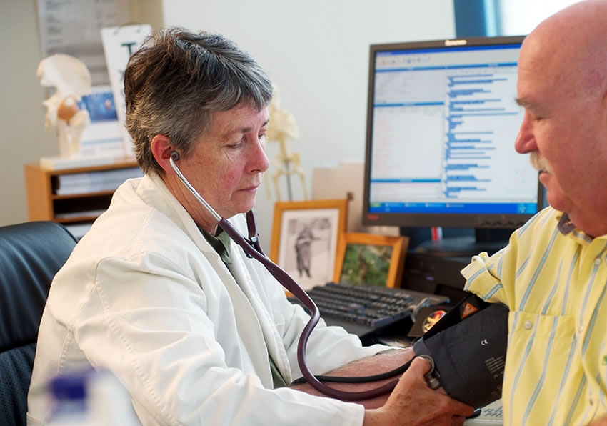 female doctor in her medical office checking male patients blood pressure 