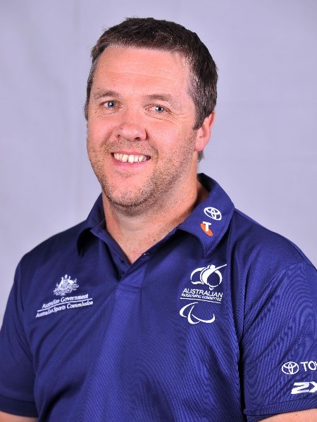 Studio portrait photo of middle aged man smiling, wearing blue T-shirt