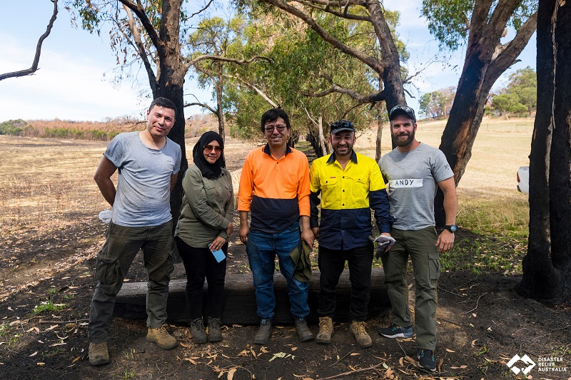 Five people smiling with trees in background. Four men and a woman with head scarf