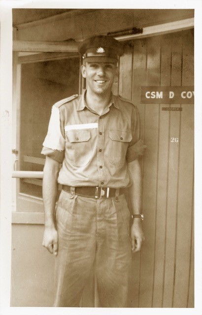 Young smiling man in uniform next to door that says 'CSM B Coy'