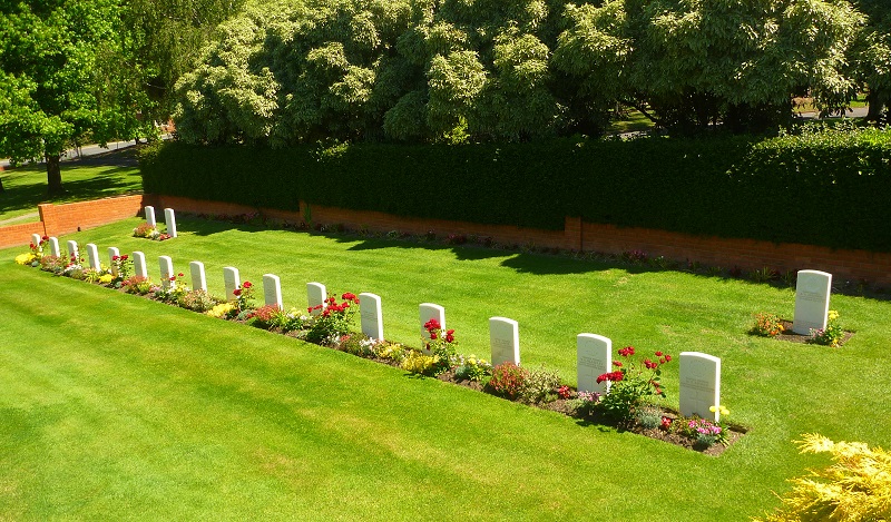 Manicured lawn with 19 white headstones and trees behind them