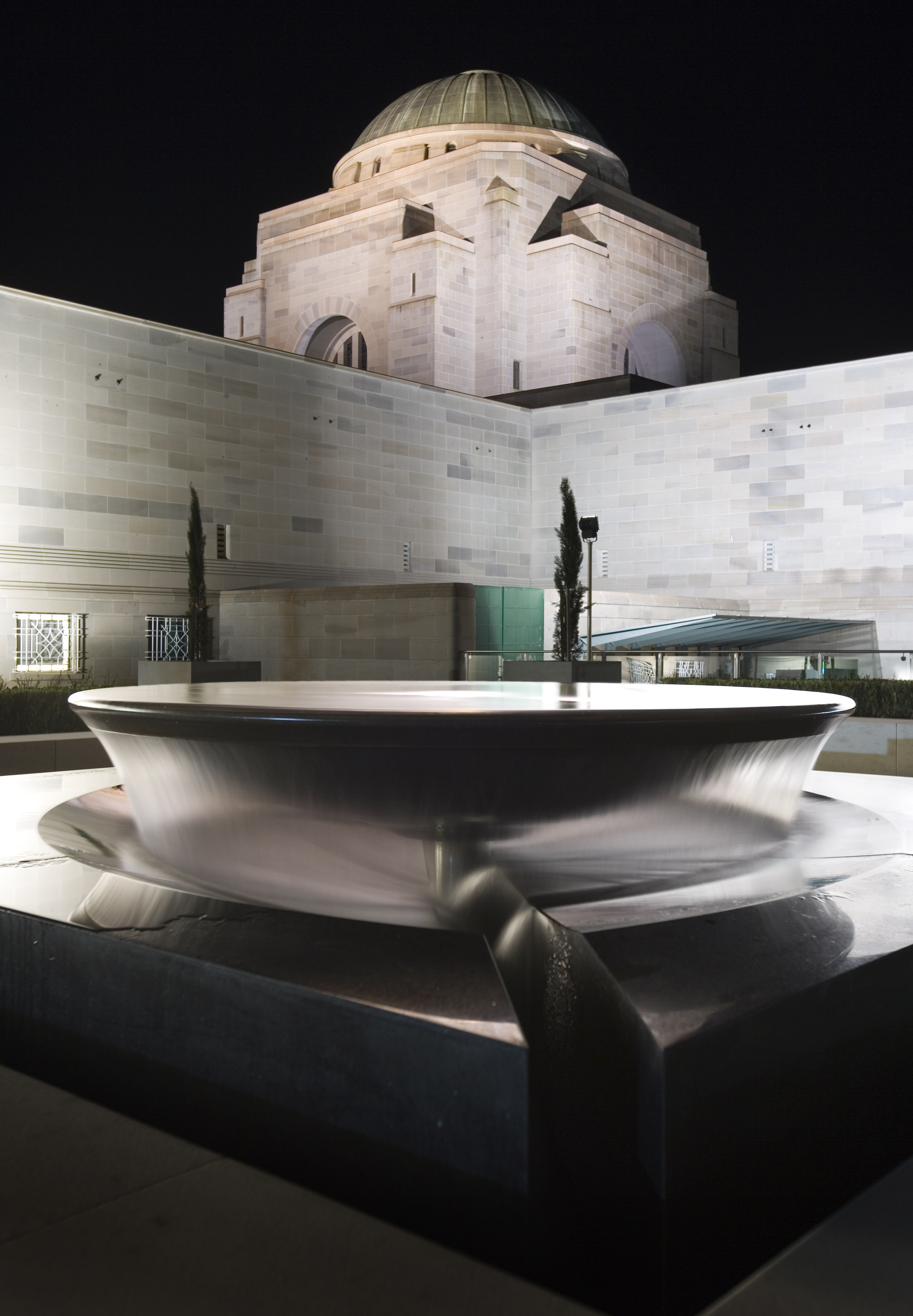 Stone dish-like sculpture at night with Australian War Memorial in background