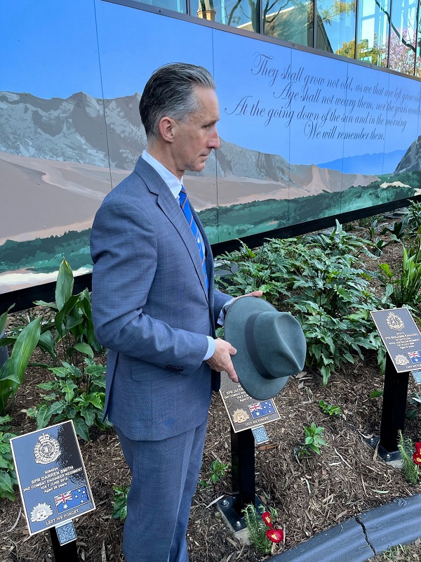 Middle aged man in suit holding hat with memorial garden in background