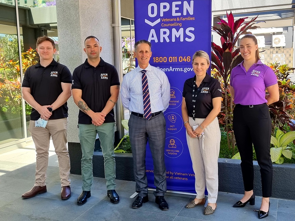 Three men and two women pose for camera with Open Arms banner behind them