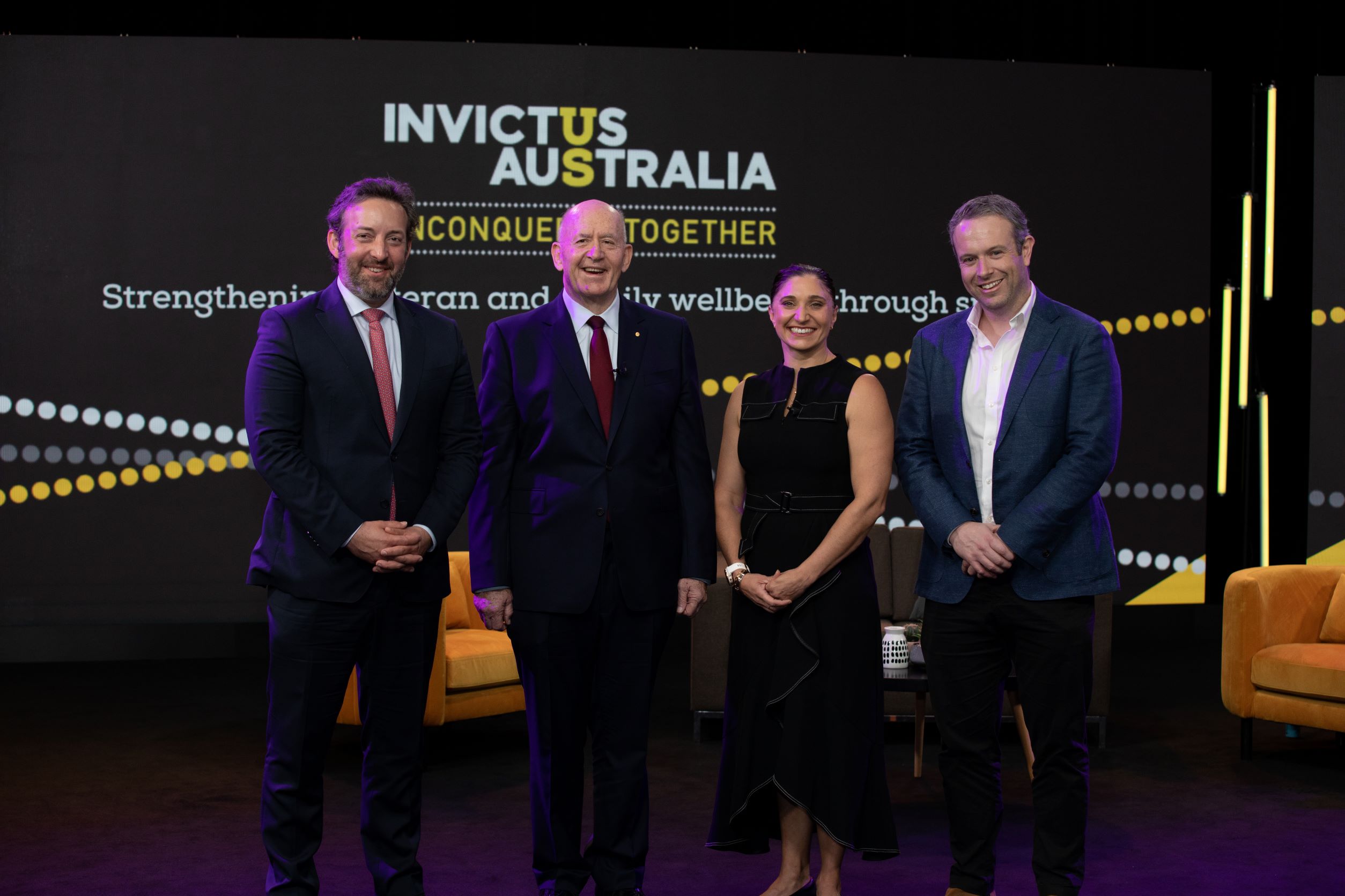 Three men and a woman posing in front of Invictus Australia signage