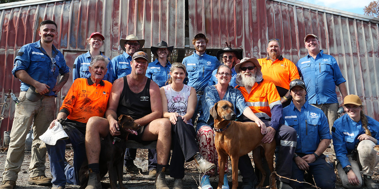 About 20 people posing for photo in front of outback shed