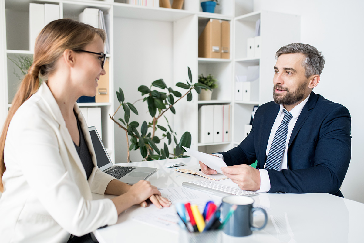 Man in suit talking to young woman at desk