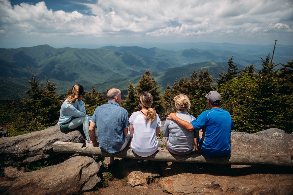 Family of five sitting on cliff top looking over view of wooded hills