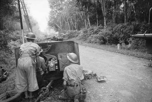 Two soldiers manning piece of artillery next to road