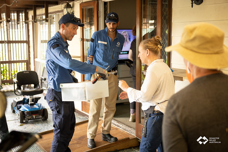 Two men in DRA t-shirts discuss a box of possessions with an elderly couple