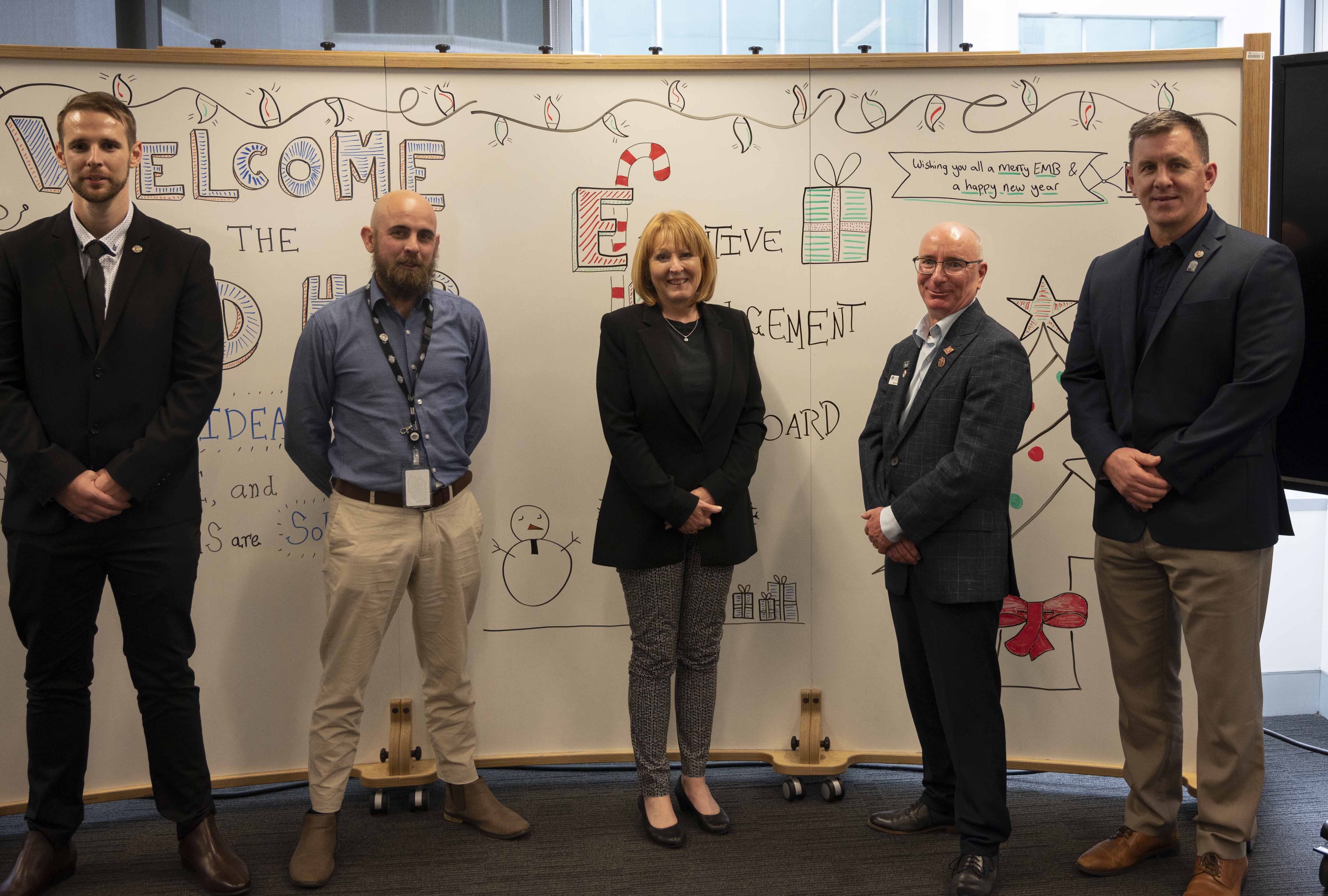 A woman and four men posing in front of  a white board