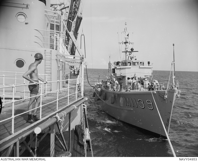 Small warship docks alongside larger Navy ship at sea, while a sailor looks on