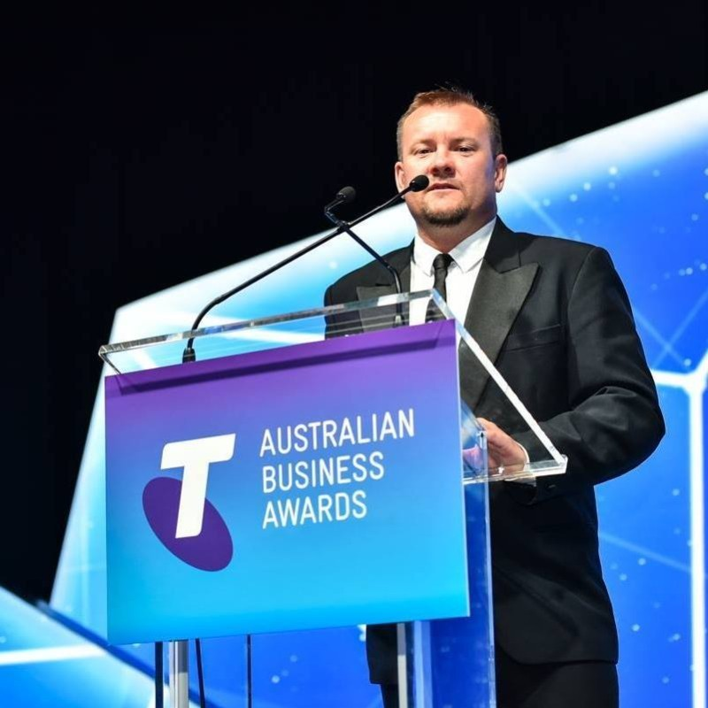 Man in suit at lectern with Telstra Australian Business Awards on it