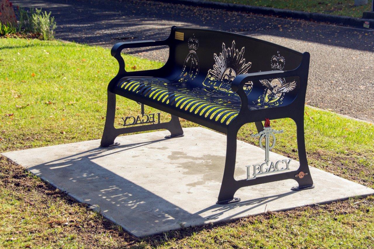 Carved metal bench on concrete platform surrounded by grass