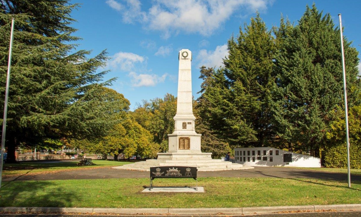 Stone cenotaph with bench on front, surrounded by grass and trees