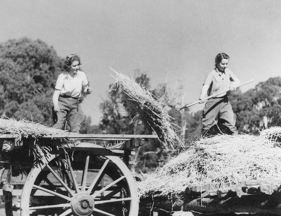 Two young women moving hay around on a cart