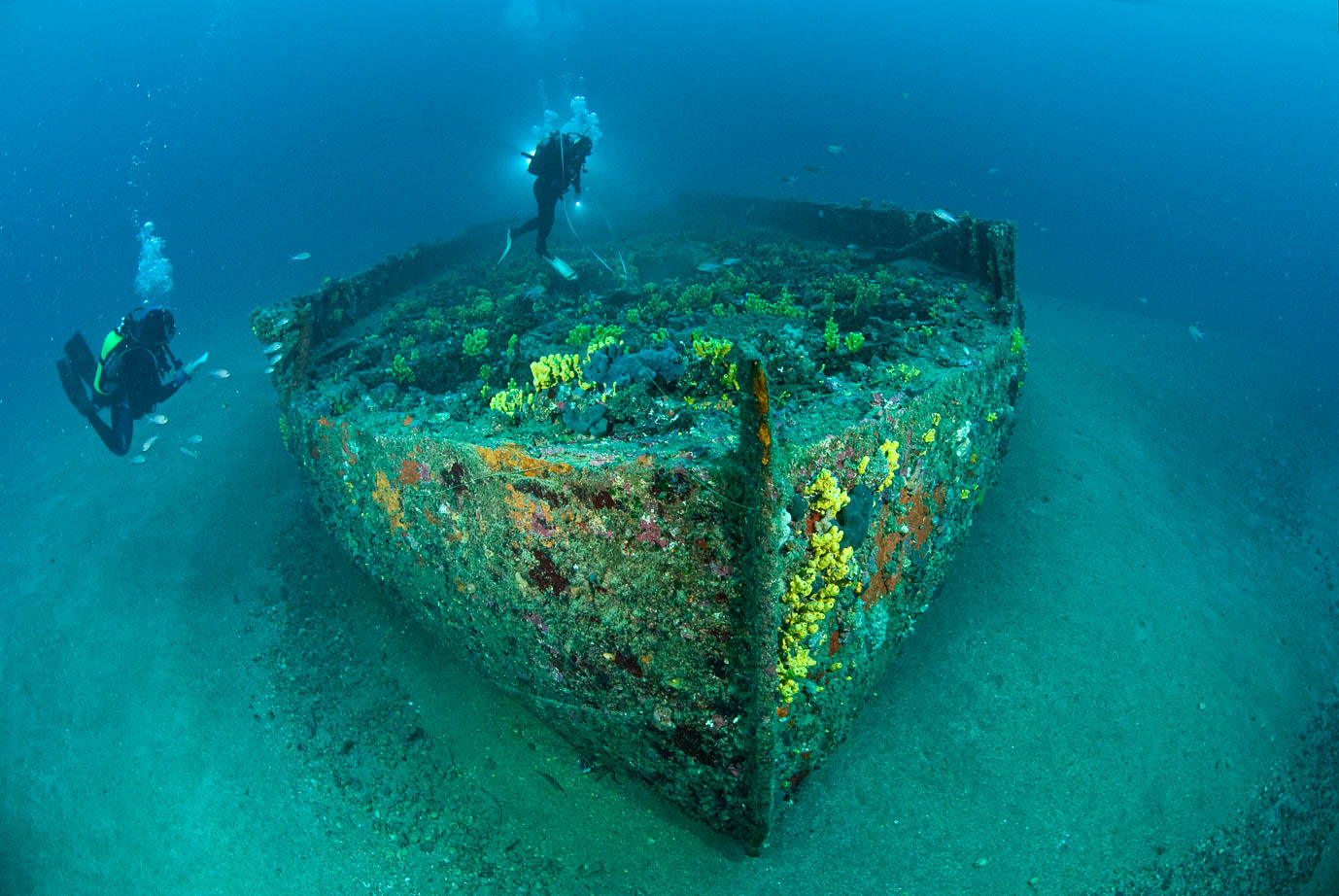 Two scuba divers inspect the remains of a long rowing boat.