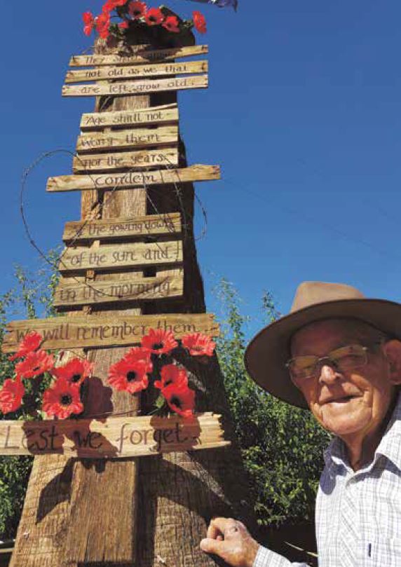 Old man next to timber post with poppies and boards with the Ode of Remembrance inscribed on them