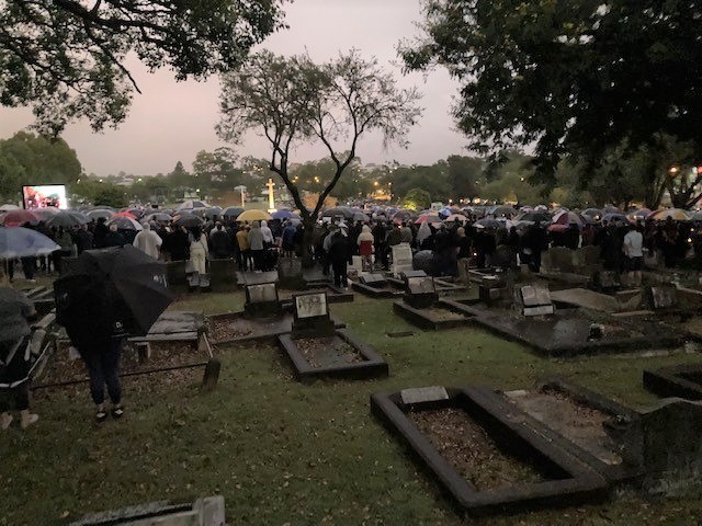 Dim photo of people with umbrellas gathered in cemetery