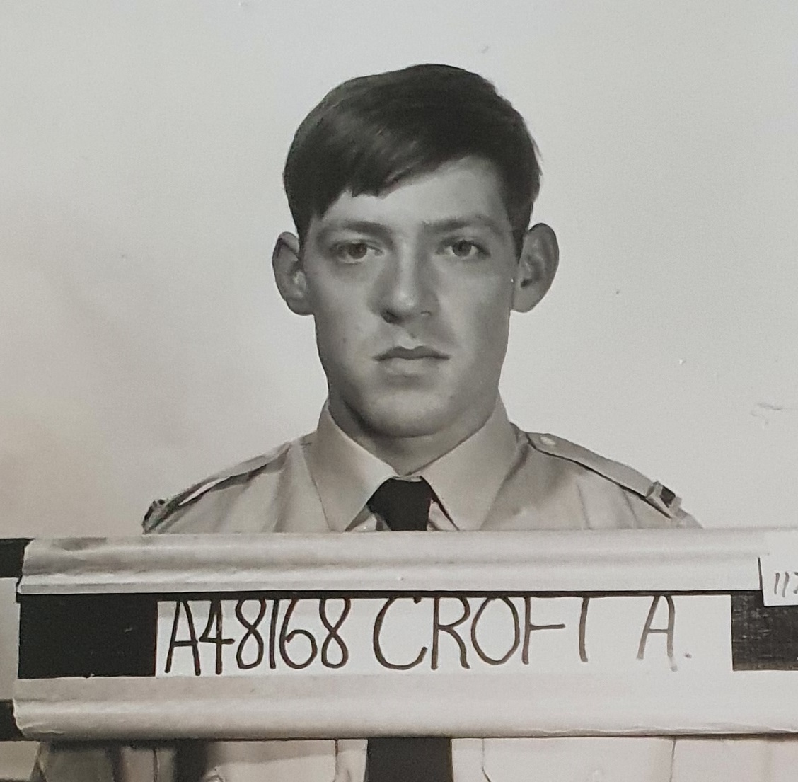 Black and white mugshot of young man in RAAF uniform with his serial number on a board.