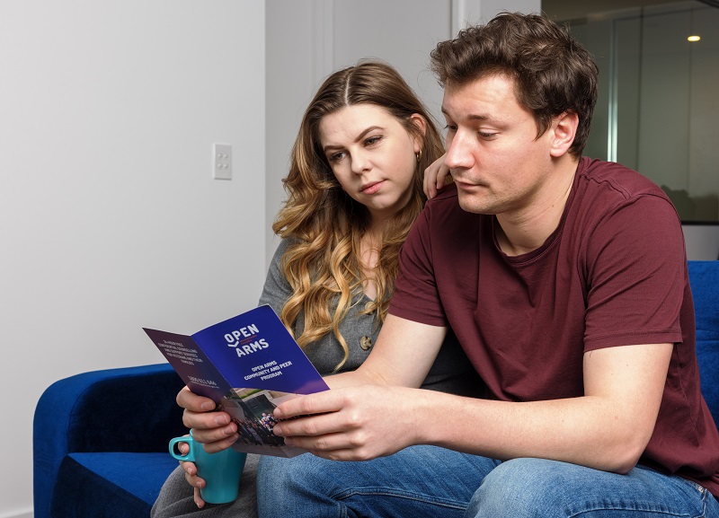 Young couple on sofa look at Open Arms brochure