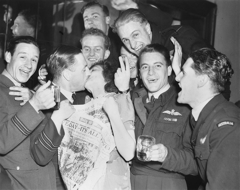 Woman kisses air force officer, surrounded by other happy, cheering air force officers