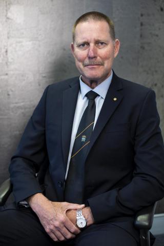 Middle-aged man sitting in front of concrete wall, posing for camera