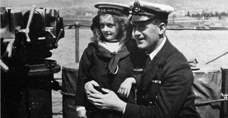 Smiling Naval officer shows little girl in sailor outfit around a ship