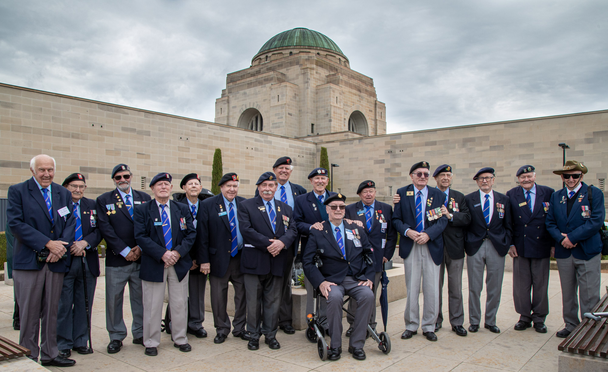 About 15 older men posing in front of Australian War Memorial