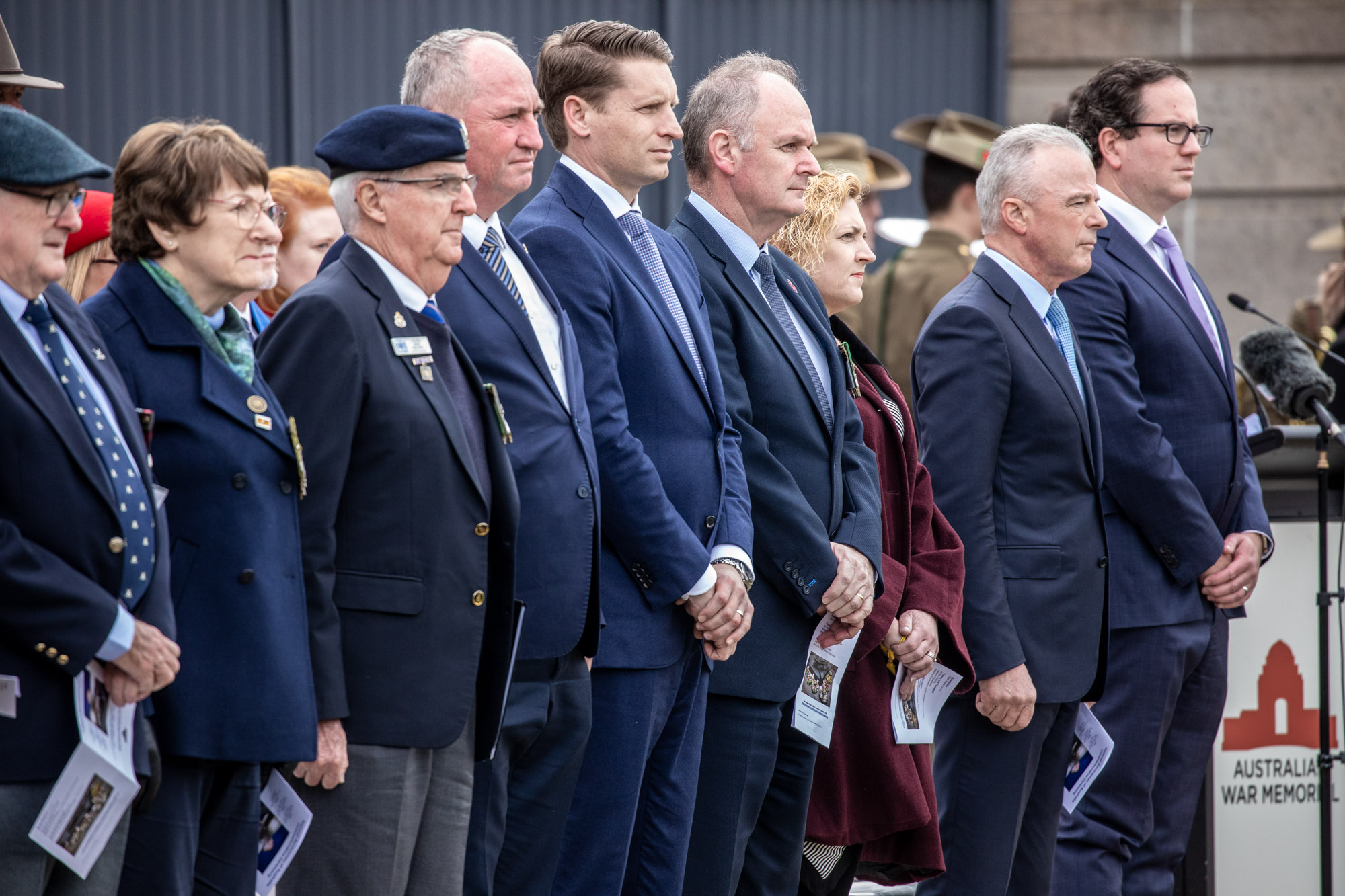 A row of mostly men in suits standing solemnly