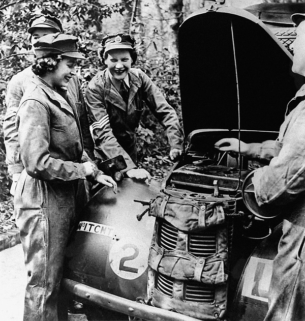 Two young women and two men contemplate the engine of a vehicle