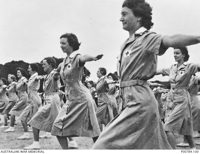 Black and white photo of dozens of young women in nursing dresses doing calisthenics