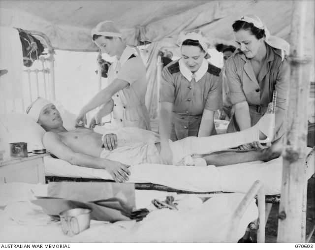 Three women in nursing uniforms attending to a wounded man on a hospital bed