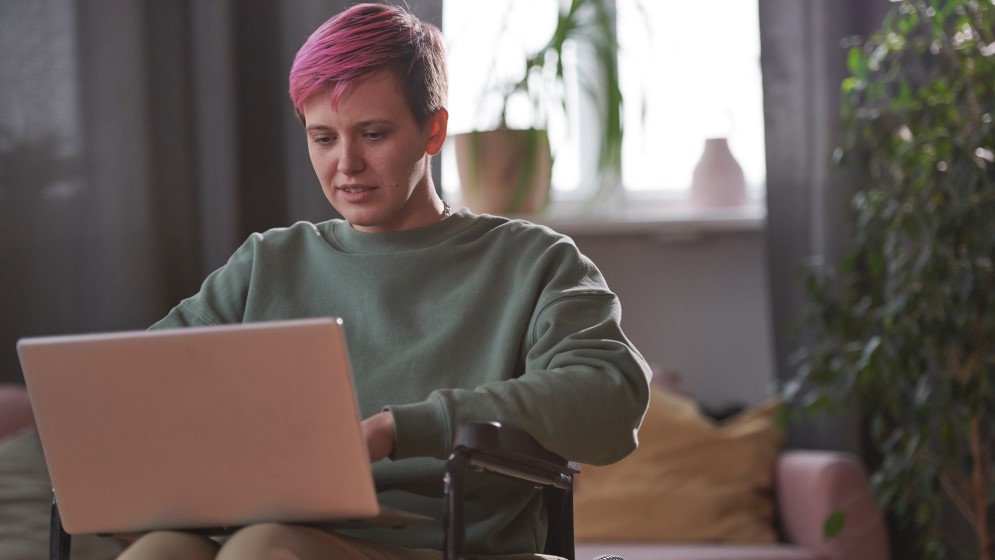 Woman with short, pink hair in wheelchair uses her laptop