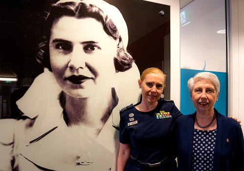 Two women standing in front of large portrait of Second World War nurse