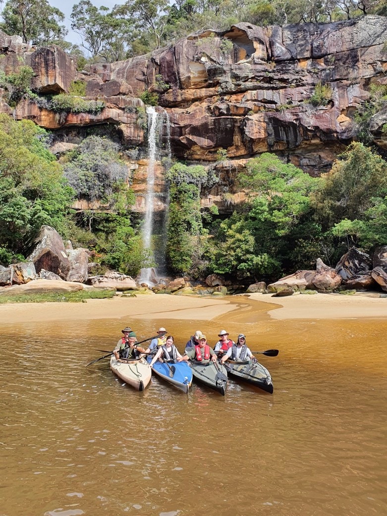 A group of people in kayaks in the water. A waterfall is in the background.