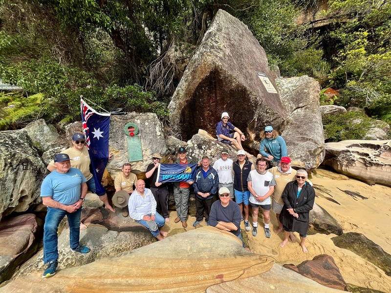 A group of people on a beach with a memorial plaque and an Australian flag.