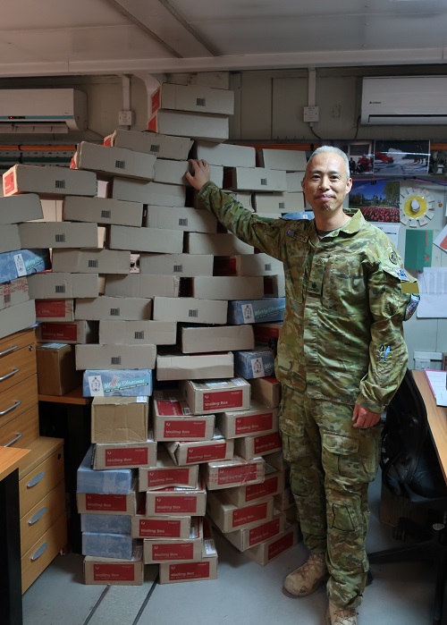 Smiling Army officer poses for camera next to pile of boxes