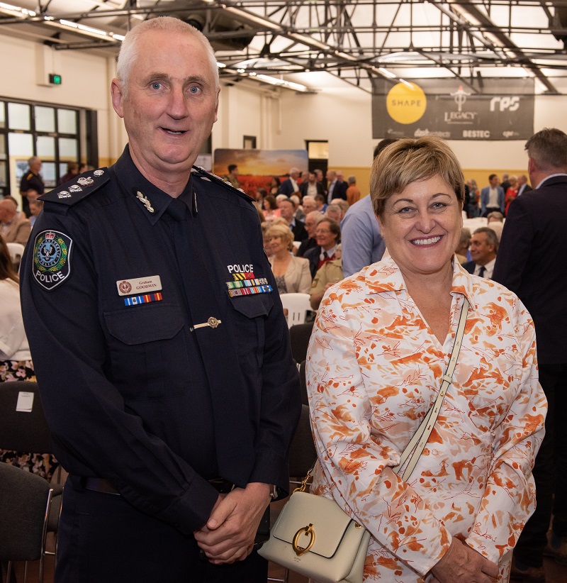 Senior police officer poses next to woman with people in background