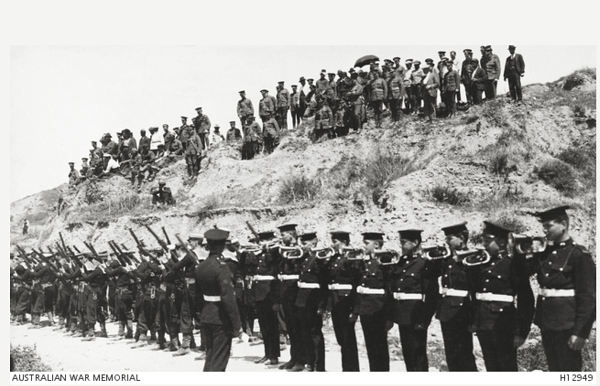 A line of soldiers with rifles pointed at the sky on a simple road, overlooked by civilians and other soldiers