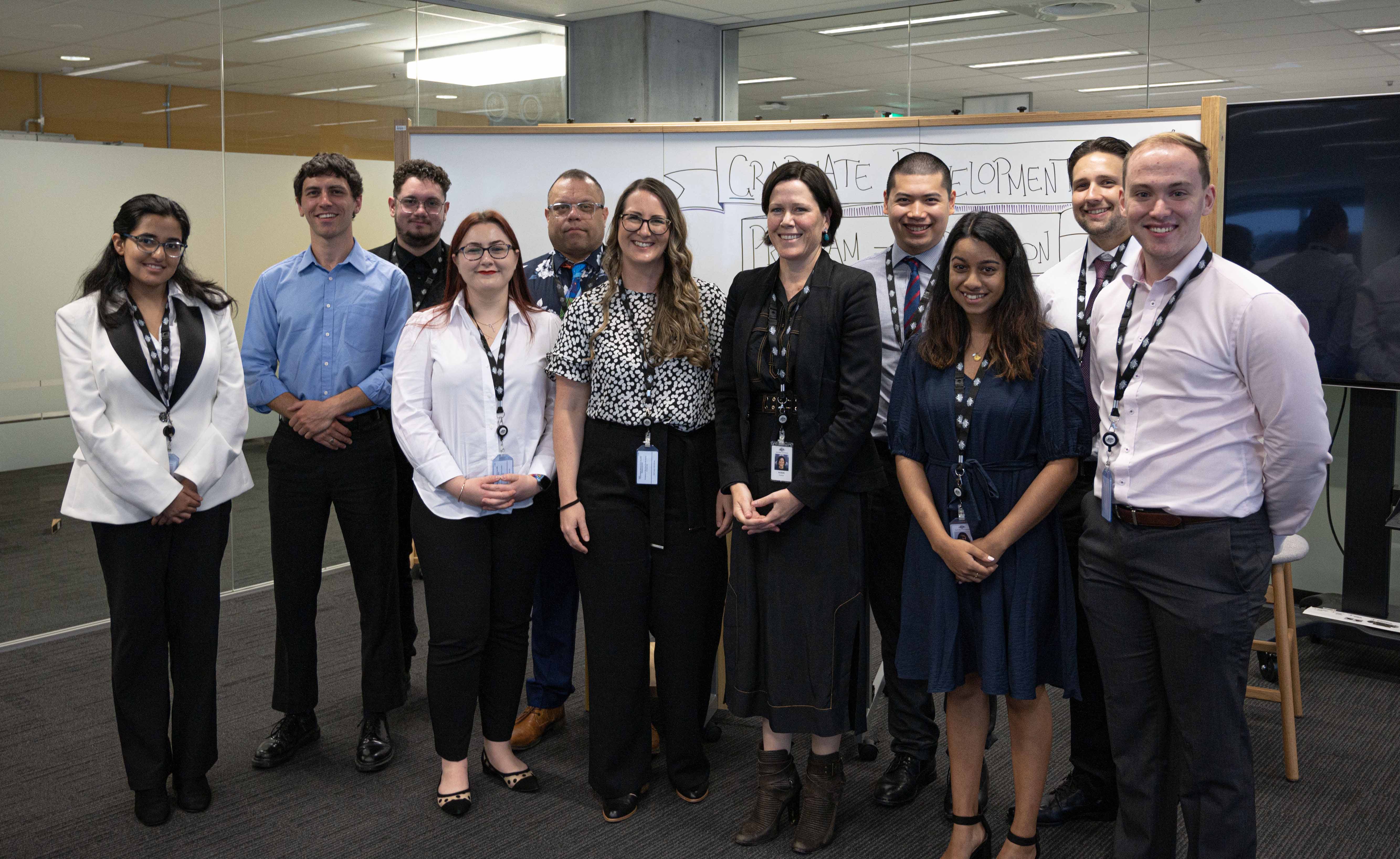 Ten people pose for camera in office, with whiteboard in background