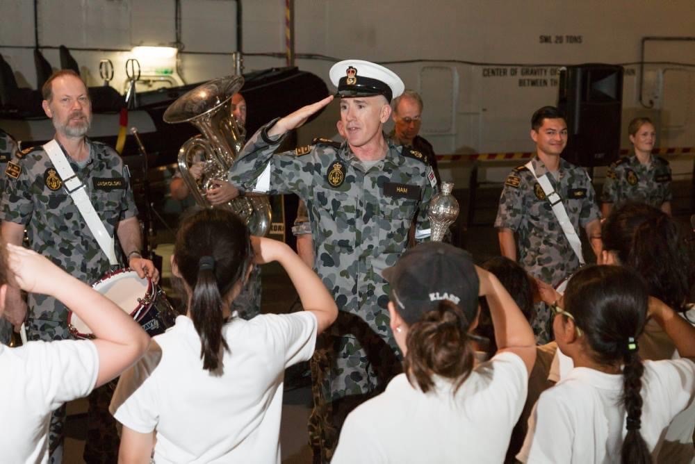 Navy warrant officer saluting to school children who are saluting in return