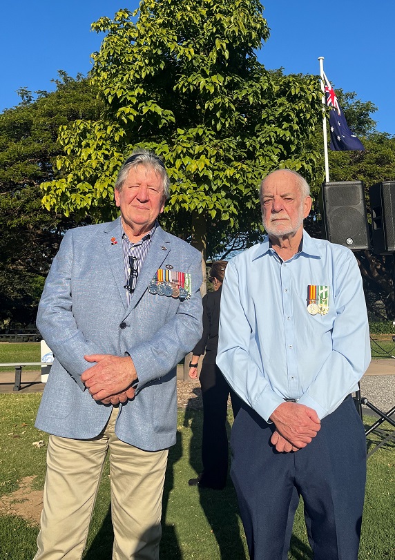 Two older men posing for camera in park. Both are wearing medals.