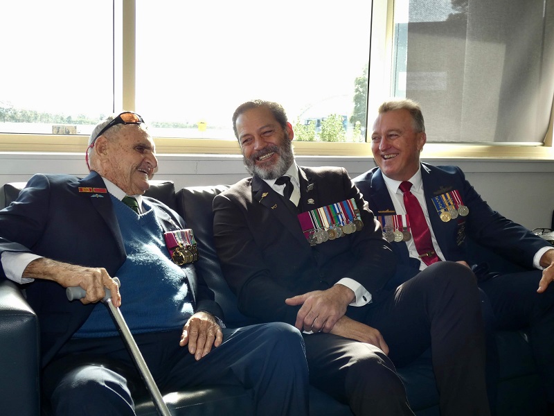 Three older men sitting on a sofa, laughing