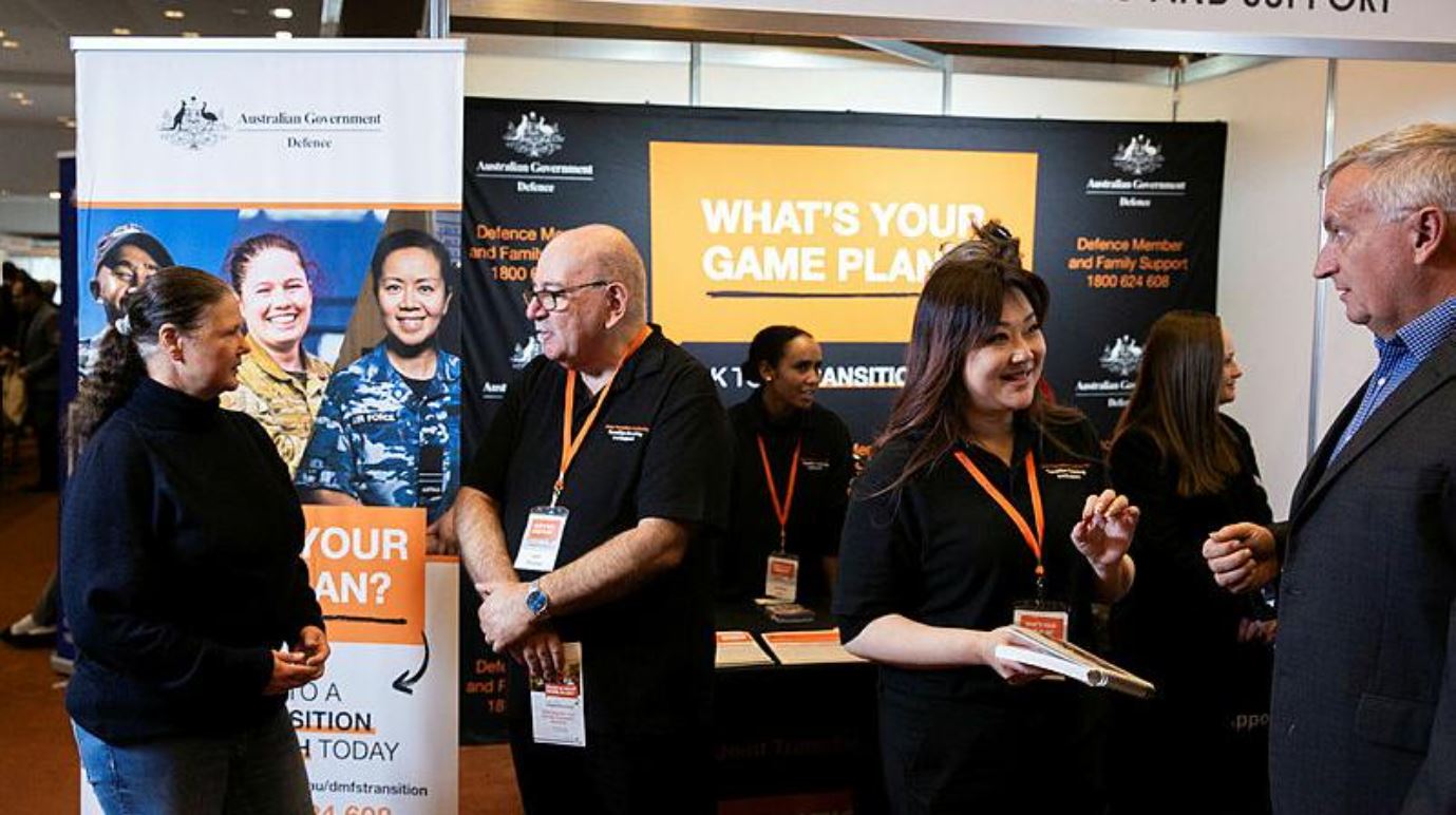 Two or three people in black T-shirts talking to people in civilian clothes at a function centre