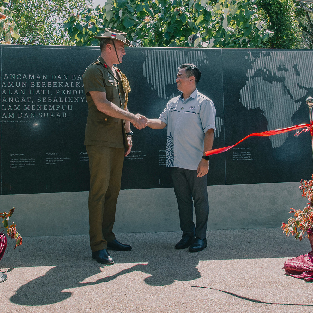 A black curved wall engraved with imagery of a world map. A soldier is shaking hands with another man in front of the memorial